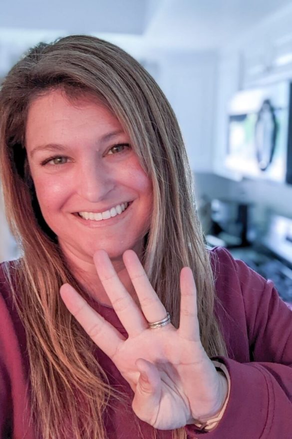 A photo of a mom in her kitchen holding up the number 4 with her fingers.